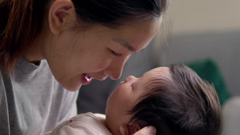 drawing closer to smell her baby's mouth, the mother of a newborn child is smiling as she looks lovingly at her sleeping child