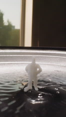 white figure of man standing in hyaluronic acid vibrating on loud speaker. liquid substance on operating sound equipment in light studio macro