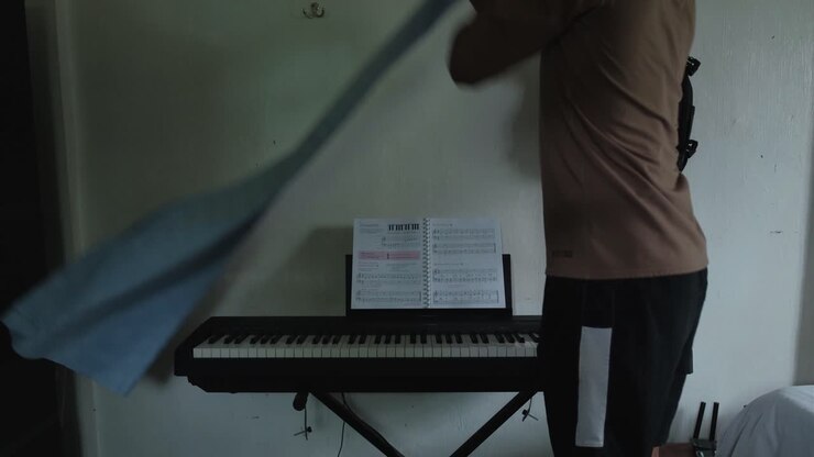 Inquadratura statica posteriore di un giovane uomo che posiziona un telo di copertura su un pianoforte elettrico a 88 tasti.