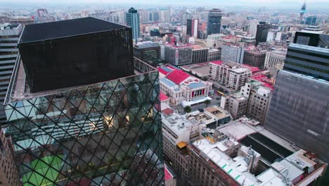 descending aerial view of a glass building in a diamond pattern in downtown santiago chile with the municipal theater in the background