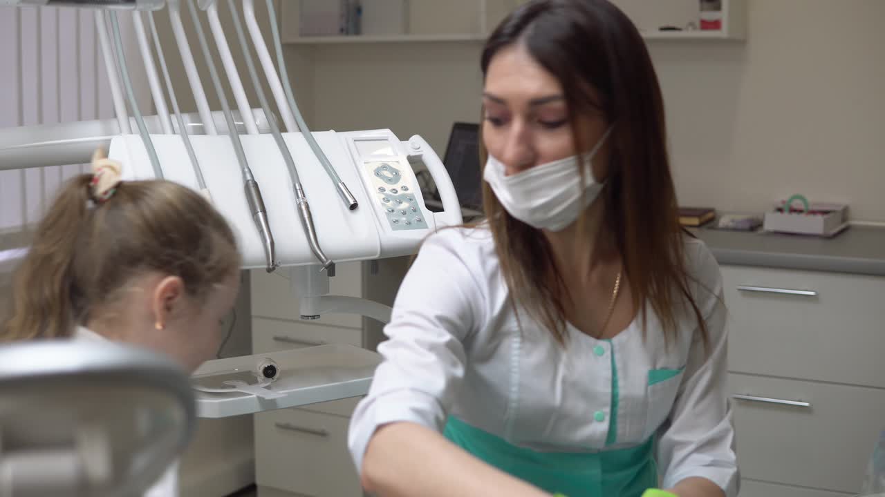 Friendly female dentist taking off a napking after procedures and giving cute little girl a beautiful green apple. Shot in 4k