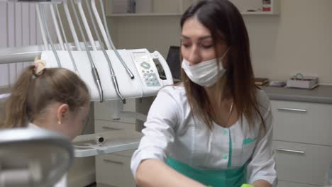 Friendly-female-dentist-taking-off-a-napking-after-procedures-and-giving-cute-little-girl-a-beautiful-green-apple.-Shot-in-4k