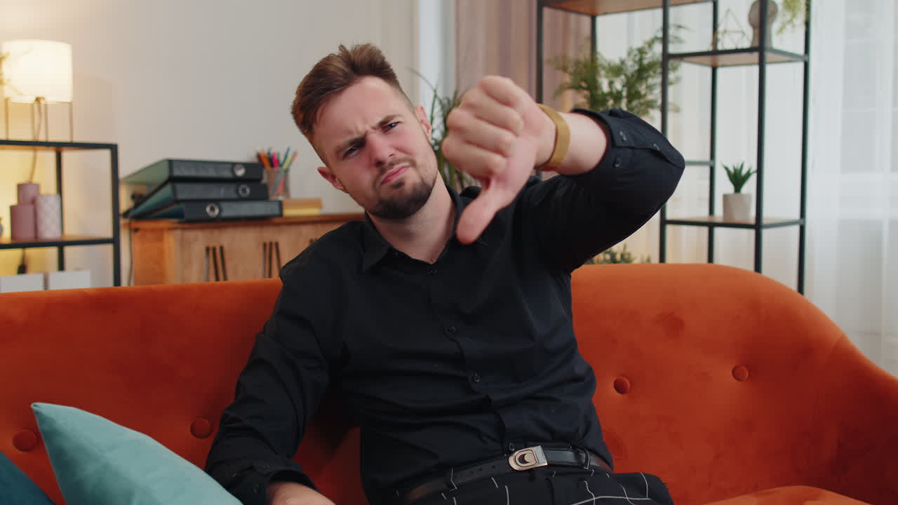 화가 난 젊은이가 엄지손가락을 내려놓고, 나쁜 일을 싫어하고, 불쾌감을 느끼고, 집에서 불만족한 피드백을 받습니다.