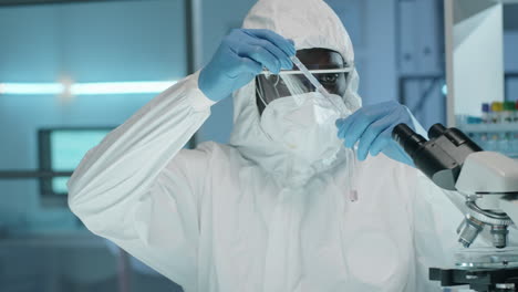 african american lab worker in protective suit doing chemical experiment