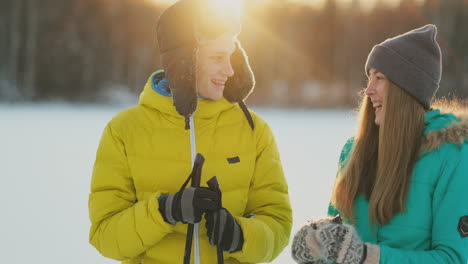 a man in a yellow jacket and a girl in a blue jumpsuit skiing in slow motion at sunset