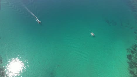 A-graceful-boat-glides-on-vibrant-crystal-blue-waters,-sails-billowing-in-a-gentle-breeze