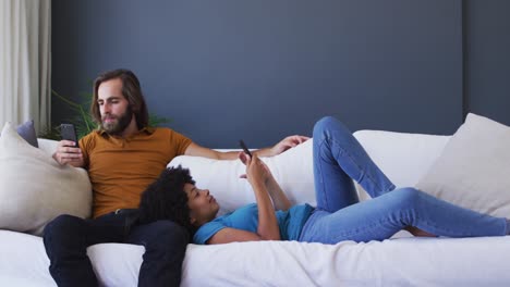 mixed race couple using smartphone on the couch at home