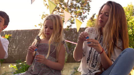 Mother-Blowing-Bubbles-With-Children-On-Blanket-In-Garden