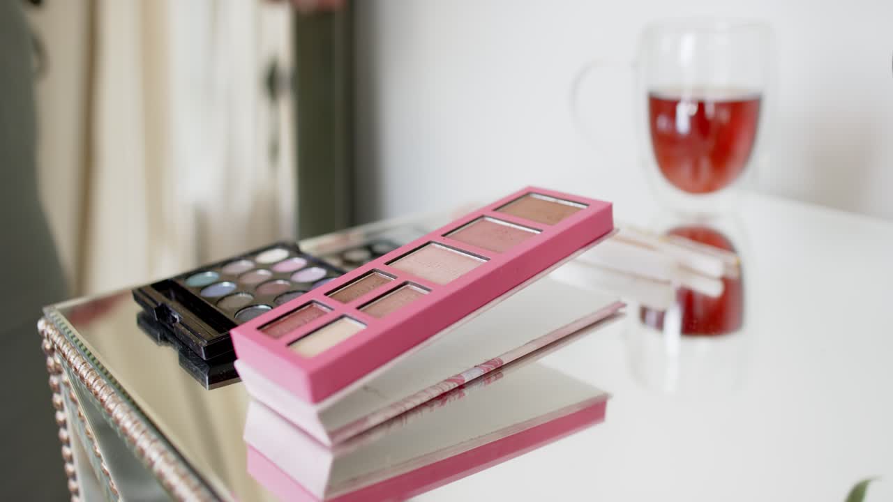 Striped-sleeved arm entering left is picking brush and tapping pink palette on vanity to pick color