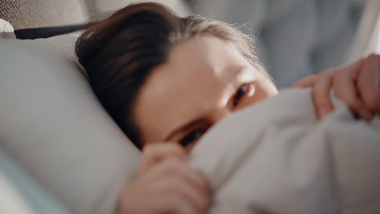 Woman hiding soft blanket in cozy bedroom closeup. Playful brunette lying pillow