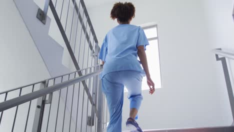 Mixed-race-female-doctor-wearing-face-mask-running-up-the-stairs-in-hospital