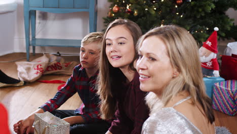 Mother-Sitting-On-Floor-With-Children-As-They-Open-Christmas-Gifts