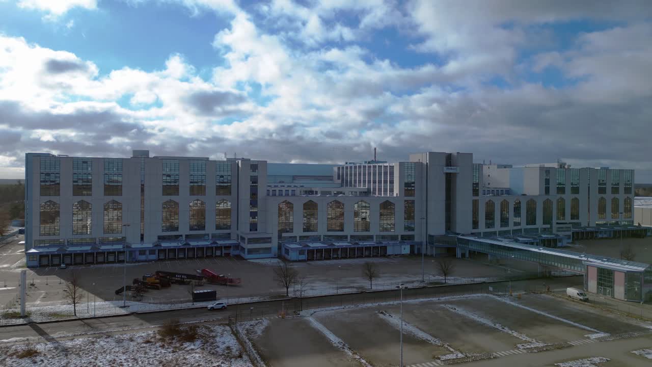 Large distribution center like an industrial castle with loading docks and parking lot under a cloudy sky in winter. Great aerial view flight ascending drone