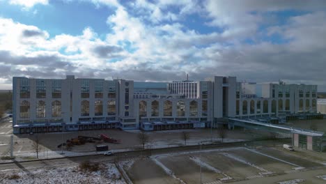large distribution center like an industrial castle with loading docks and parking lot under a cloudy sky in winter. great aerial view flight ascending drone