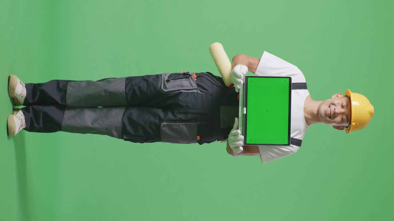 Full Body Of Asian Man Painter Wearing Safety Helmet Smiling And Showing Green Screen Laptop To The Camera While Standing In The Green Screen Background Studio
