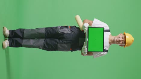 full body of asian man painter wearing safety helmet smiling and showing green screen laptop to the camera while standing in the green screen background studio