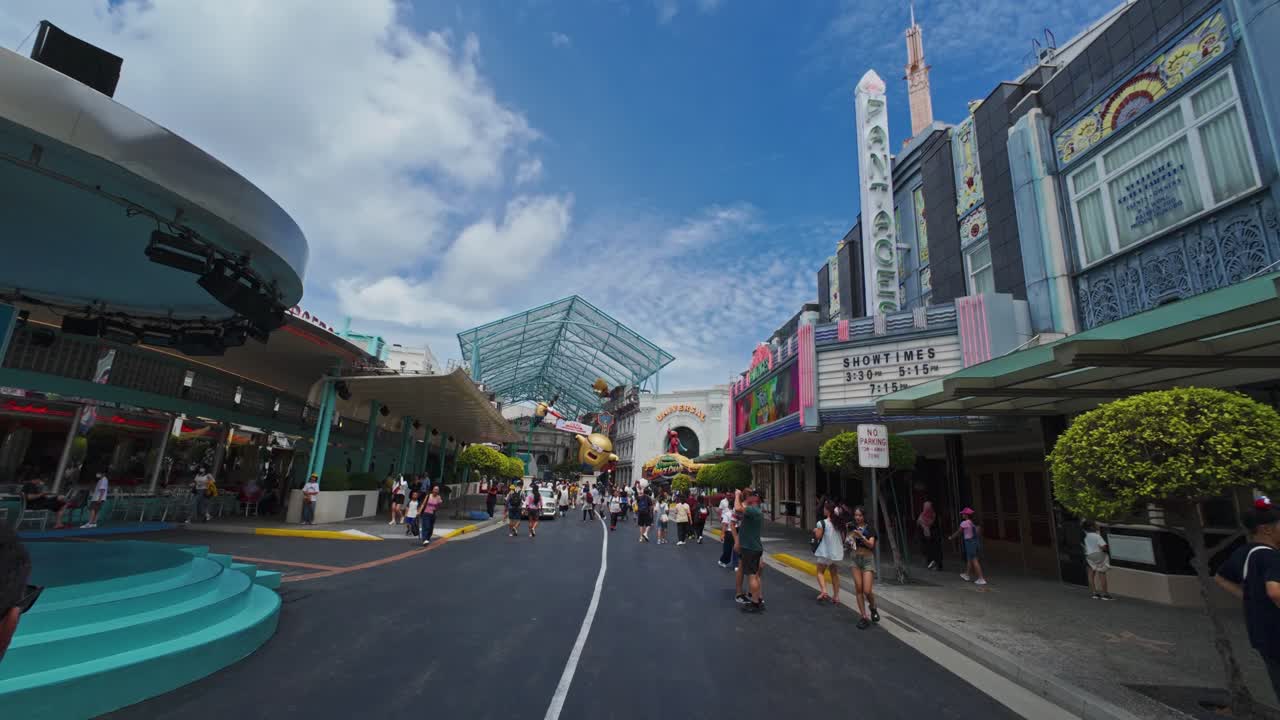 Theme park visitors walk through Universal Studios under a bright blue sky