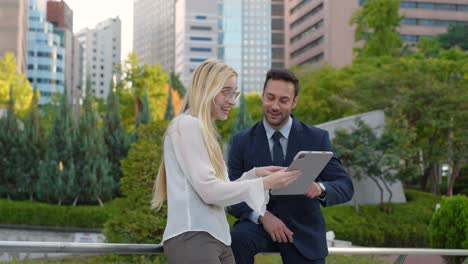two young business people sharing ideas outdoor. woman presenting project in digital tablet. medium shot, slow motion