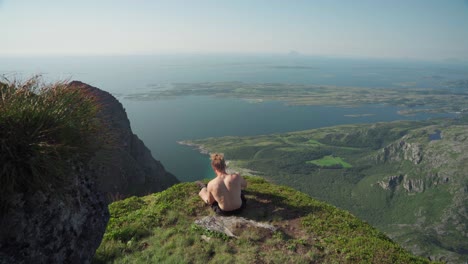 shirtless hiker sitting and taking pictures from donnmannen in norway