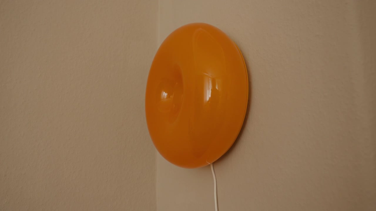 Side view of a retro orange wall lamp on a neutral interior wall, a warm design detail for decor, lighting and vintage styling themes.