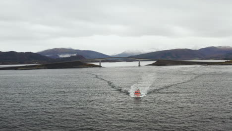 boat cruising at norwegian sea with storseisundet bridge in background in norway