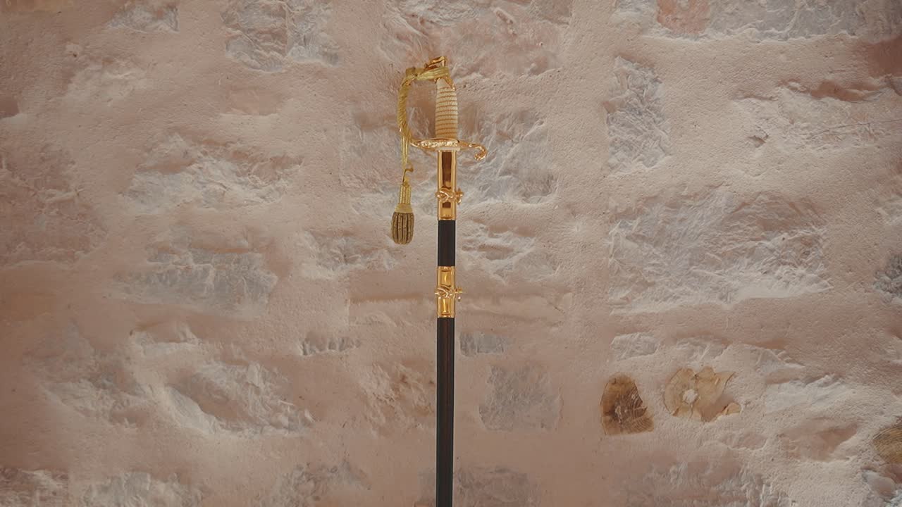 Spada navale dorata su parete di pietra, esposizione elegante e storica.