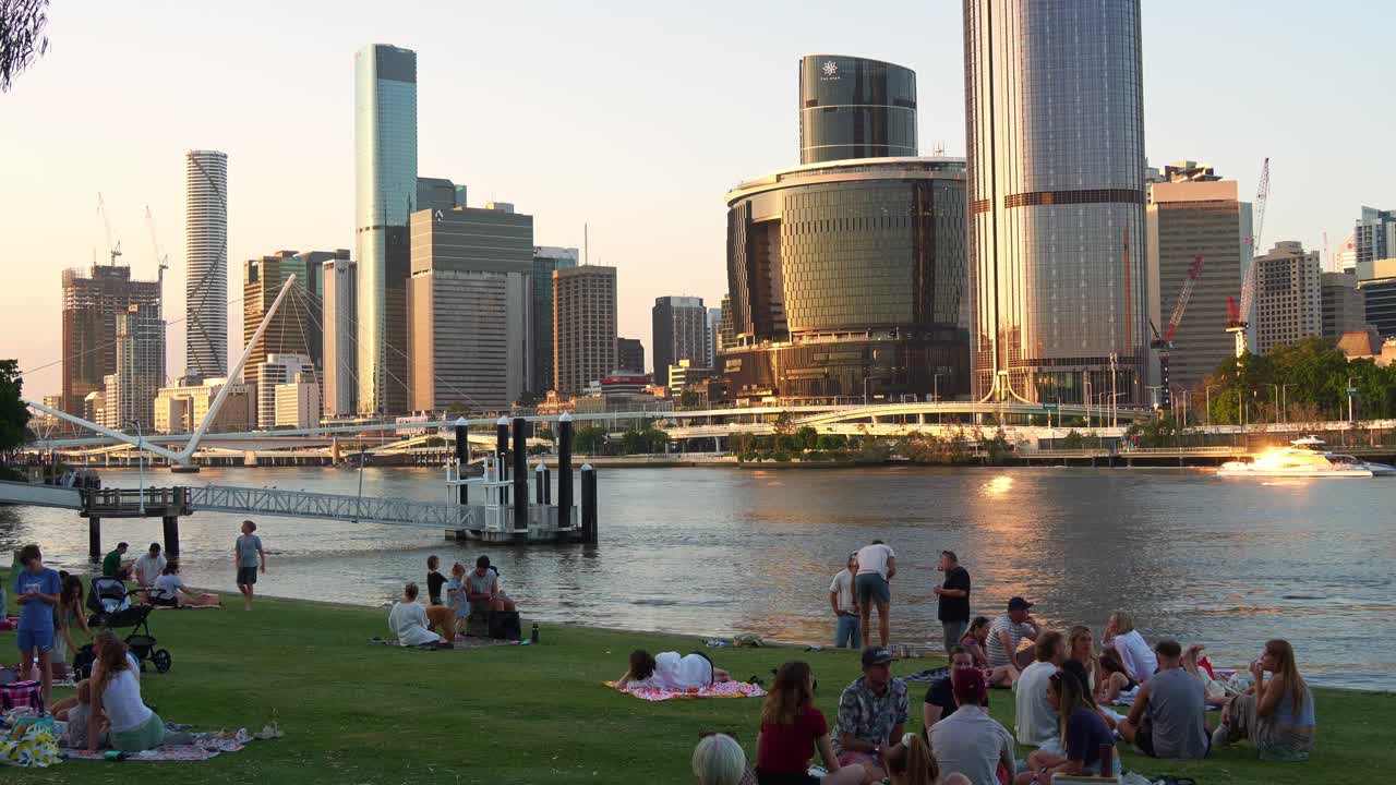 Time-lapse shot capturing family and friends gather for a picnic on River Quay Green, South Bank on the weekend, overlooking at Brisbane river and downtown cityscape at sunset.