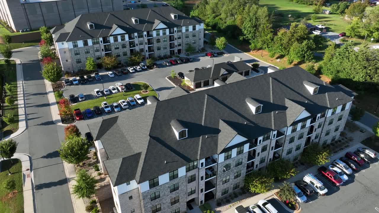 Parkerede biler ved lejlighedskomplekser i en amerikansk by. Moderne arkitektur med gråt tag på en solskinsdag i efteråret. Top-down luftfoto baglæns. Fredfyldt fællesskabsscene