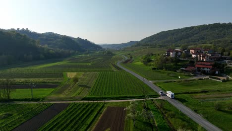 camper driving on rural road in farmland valley - drone view track