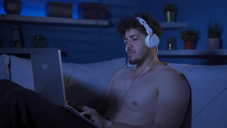 un joven somnoliento y agotado mirando su computadora portátil.
