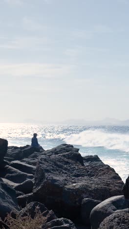 person sitting on rocks by the ocean