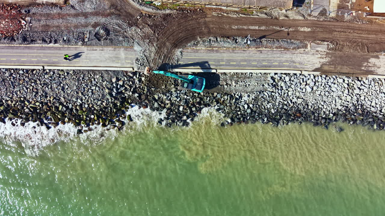 Lavori di costruzione su una strada lungo l'acqua mentre macchinari pesanti spostano rocce e materiali sul litorale in un'area costiera