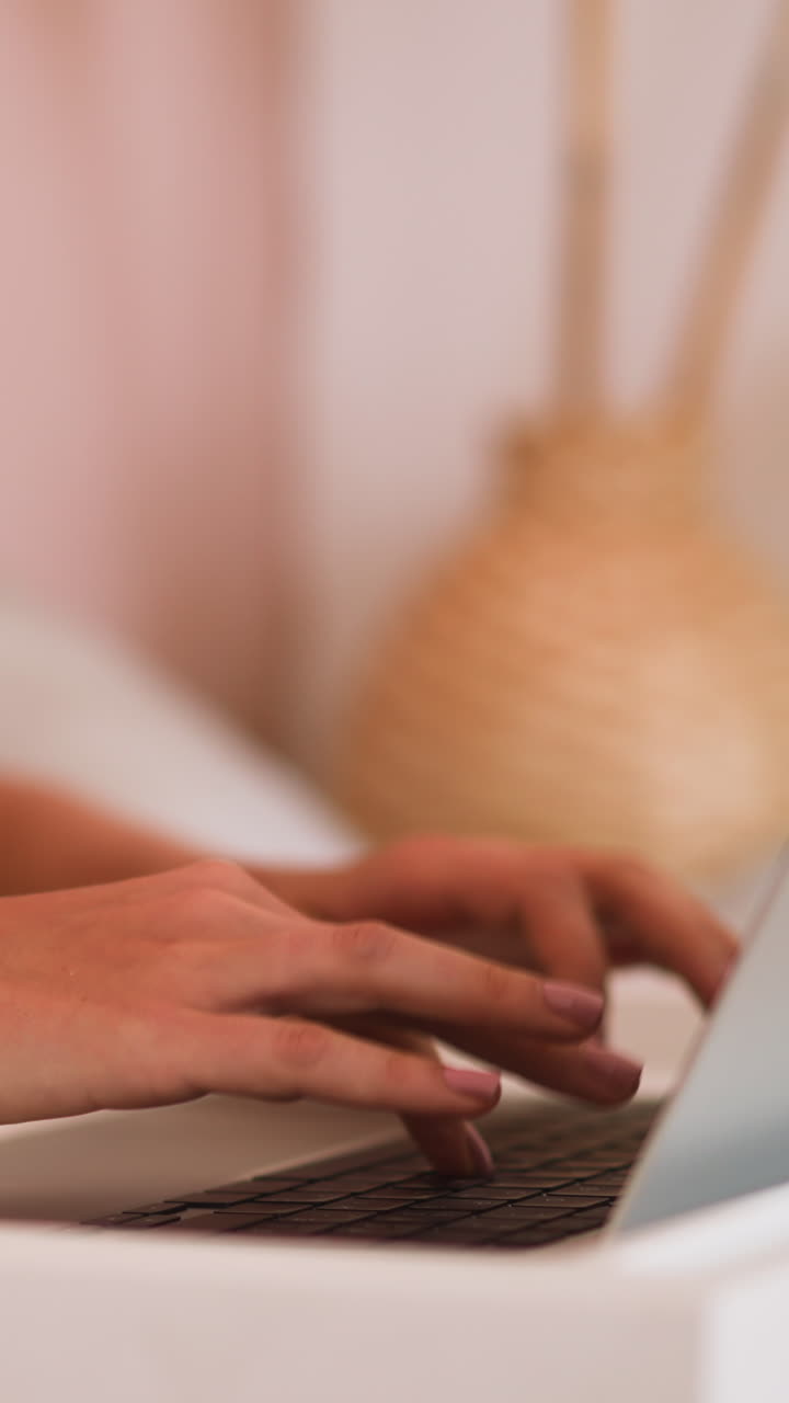 Young woman types message on keyboard of modern laptop put on bed breakfast table sitting comfortably on blurred background slow motion closeup