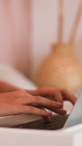 young woman types message on keyboard of modern laptop put on bed breakfast table sitting comfortably on blurred background slow motion closeup
