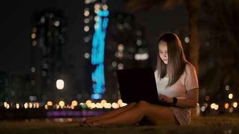 young beautiful girl designer working remotely on a laptop on the street in the summer under palm trees at night in the city park. united arab emirates european woman at night in dubai
