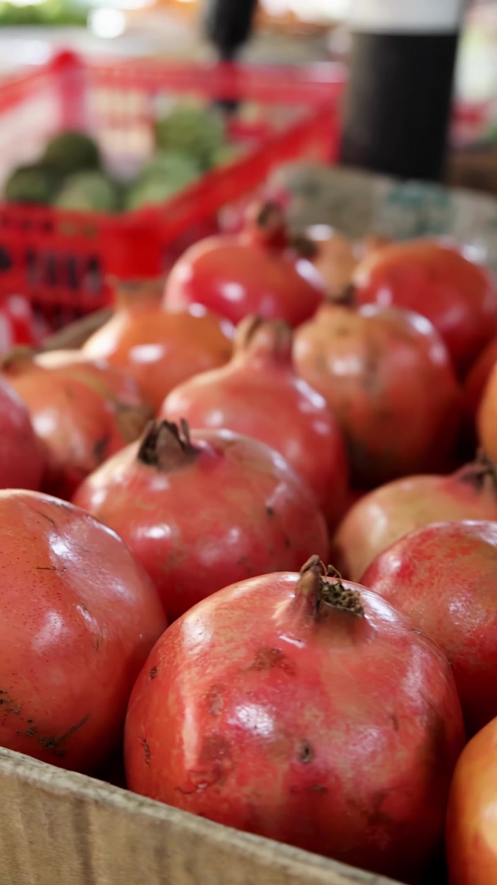 Nærbillede af kamerabevægelse hen over kurve med granatæbler, sapodillaer og guavaer på et livligt udendørs grøntsagsmarked med naturligt dagslys og lav dybdeskarphed.
