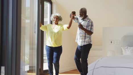happy senior diverse couple dancing in living room at retirement home