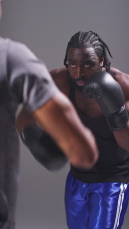 vertikale video-studio-aufnahme eines männlichen boxers, der mit einem trainer trainiert, der schlaghandschuhe oder handschuhe trägt und für den kampf 1 übt.