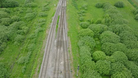 vista aérea a vista de pájaro de vías de tren de ferrocarril vacías, paisaje rural, bosque verde fresco en el lado, día de verano nublado y nublado, amplia toma de avión no tripulado avanzando