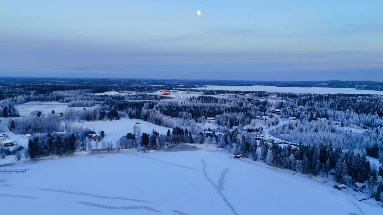 Frossen innsjøbredd med landsby under fullmåne, Lappland, Finland. Forhøyet droneutsikt over islagt innsjø