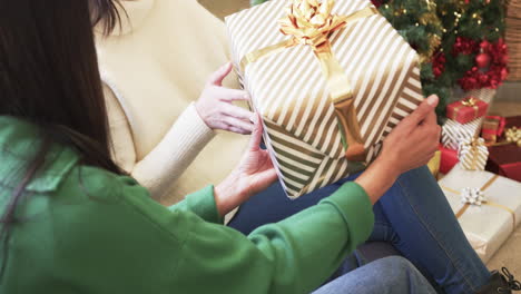 midsection of biracial mother and adult daughter exchanging christmas gift at home, slow motion