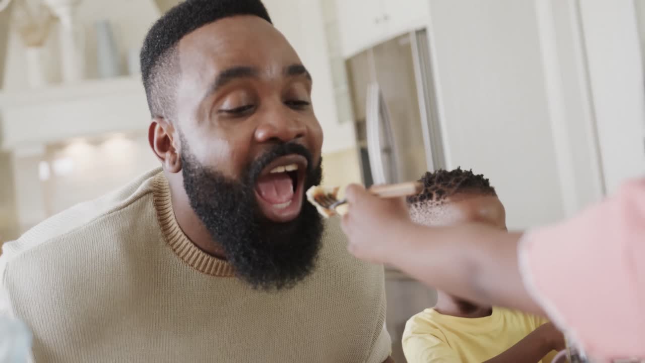 Lykkelig afroamerikansk far med sønn og datter som nyter et måltid i spisestuen, sakte film.
