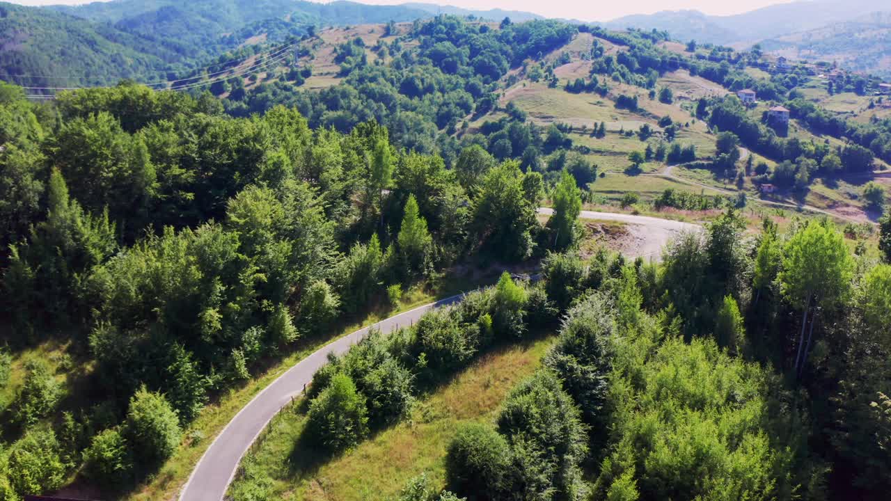 seguir a través de una toma de dron de un vehículo que se mueve en una carretera sinuosa en las montañas de rodope, con vistas a un hermoso paisaje de valles y pueblos en bulgaria