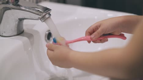 little girl cleans toothbrush with water in light bathroom