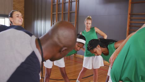 Diverse-female-basketball-team-stretching-with-male-coach