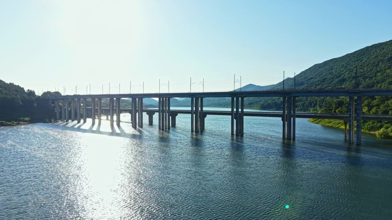 明るい日中、澄み切った青空の下、背景に山々が見える川にかかる橋