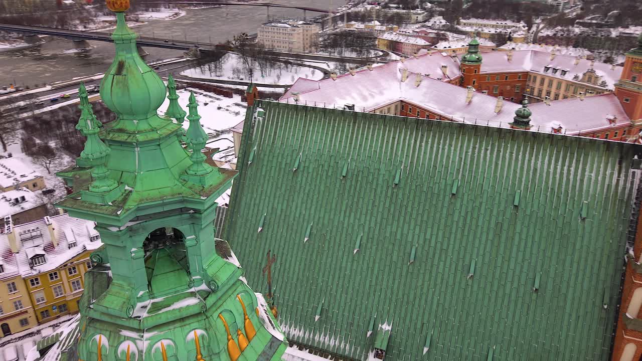 Captivating aerial footage flying by the jesuit church tower, revealing warsaw's snowy old town, the vistula river, and historic architecture