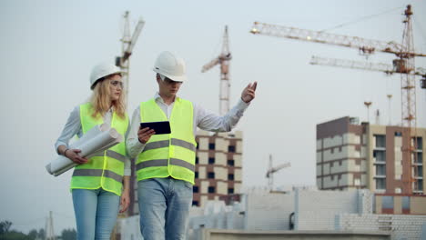 Zwei-Wirtschaftsingenieure-Tragen-Schutzhelme-Und-Halten-Ein-Tablet-In-Der-Hand.-Sie-Arbeiten-Als-Ingenieure-Und-Besprechen-Die-Inspektion-Von-Zeichnungen.-Draußen-An-Einem-Gebäude.-Technische-Werkzeuge.