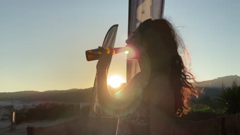 young woman drinking beer with the sunset behind in the beach-