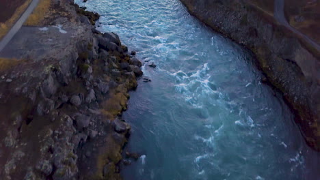 Drone-view-of-rushing-river-tilts-up-to-reveal-Godafoss-Waterfall-in-Iceland